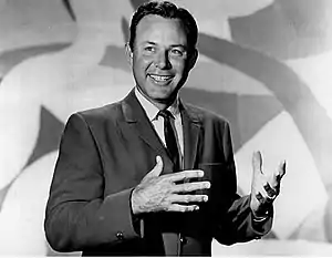 A dark-haired man wearing a jacket and tie, smiling broadly