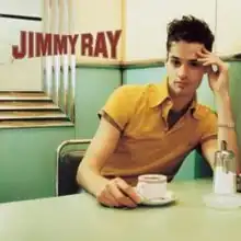 The cover features the artist at a diner, wearing a light orange t-shirt with the buttons open, showing a brown shirt under it. He has his left hand on the side of his forehead and his right hand next to a coffee cup on a saucer plate. The artist's name appears on the left side of the cover.