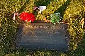 A flat, bronze grave marker surrounded by grass and decorated with flowers and small American flags