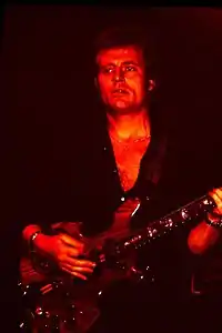 A red tinged photograph of John Paul Jones playing a bass guitar