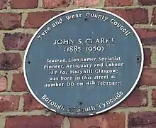 A blue plaque with the text "John S. Clarke (1885-1959) Seaman, Lion-tamer, Socialist Pioneer, Antiquary and Labour MP for Maryhill Glasgow; was born in this street at number 66 on 4th February."