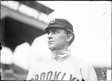 A man wearing a baseball cap and jersey with "Brooklyn" written across the chest looks–the left.