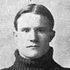 A young white man, cleanshaven, wearing a turtleneck sweater; his hair is center-parted and short