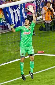 Goalkeeper John McCarthy in a green Philadelphia Union jersey, jumps while in front of an empty goal with his left arm raised.