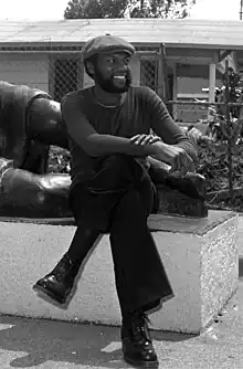 Photograph of an African American male wearing a beret and sitting at the base of a sculpture