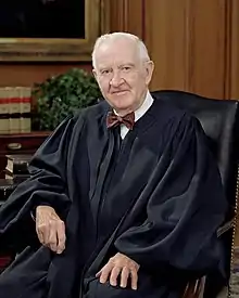 An older man with white hair wearing a black robe and a bow tie