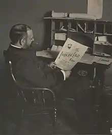 John Philip Sousa seated at a desk and looking at "The Invincible Eagle March" sheet music