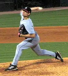 A man in a gray baseball uniform and black cap prepares to throw a baseball from his right hand as he stands on the pitcher's mound.