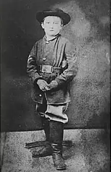 Boy wearing Union uniform, hat, and boots, looks into the camera.