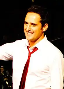 A man smiling, wearing a white shirt and a red tie.