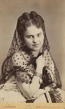 Photograph of a young woman with pinned up hair wearing a white dress and a partially transparent scarf