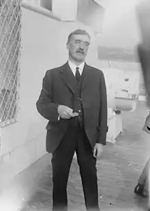 Three-quarter length photograph of a moustachioed man standing on the deck of a ship