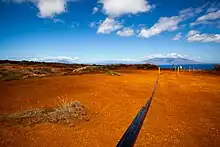 Irrigation tubing running along the red dirt of Kahoʻolawe as a crew works to plant new life in the hard packed soil