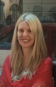 Caucasian woman with shoulder-length blonde hair wearing a red shawl