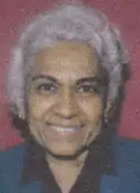 The face of an older South Asian woman with short white hair. She is smiling.