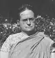 A middle-aged white woman with hair braided across her crown. She is wearing eyeglasses and a sari.