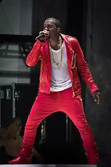 Photograph of Kanye West in a red suit and white shirt holding a microphone