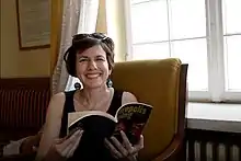 Woman smiling while sitting, holds her book of poetry near the window