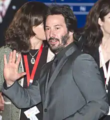 Reeves, dressed in a grey suit, waving to the crowd at the Berlin Film Festival, February 2009