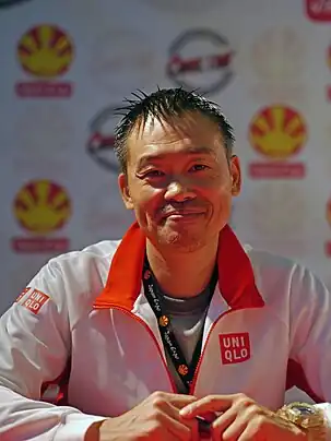 A black haired man smiling. He wears a white shirt.