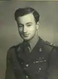male in uniform tunic, collar and tie no headress on his leftbreast can be seem medal ribbons and SAS pattern parachute wings. He is also wearing a Sam Browne belt