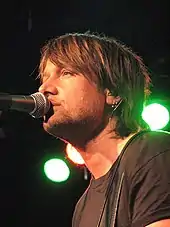 A brown-haired man singing into a microphone