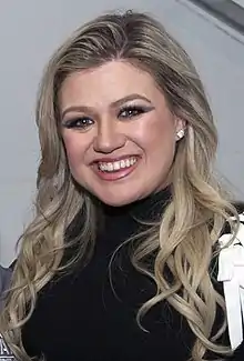 A color photograph of singer Kelly Clarkson, peering into a nearby camera.