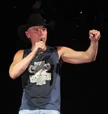 A man in a cowboy hat and dark singlet holding a microphone