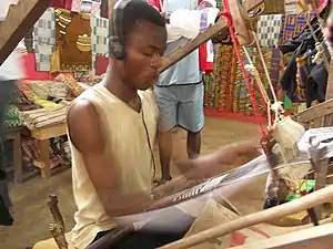 A man weaves Akan Kente cloth using a traditional loom while listening to music, Bonwire village, Ejisu-Juaben Municipal District, Ashanti Region, Ghana.