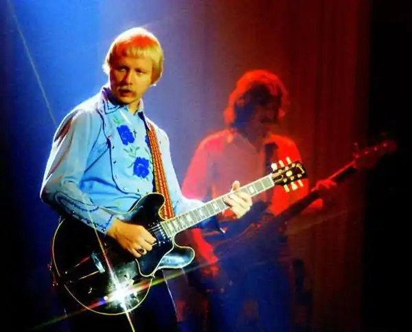Kerry Livgren performing with an electric guitar, with a band member in the background