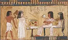 Two figures seated at the right face a standing woman and man across an offering table