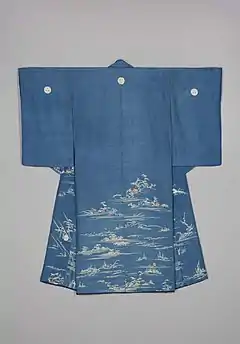 A medium blue figured silk kimono with a red lining viewed from the back. It has medium length sleeves and three crests, one in the centre back and two on each shoulder. The kimono is decorated on the waist down with designs of water, riverbanks, hills and trees in white, with small houses depicted in beige and brown.