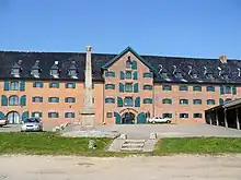 A wide brick building with a tall pillar in front.