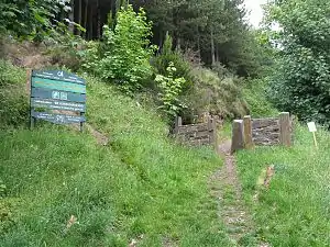 An entrance sign to the woodland, surrounded by grass and trees in the background