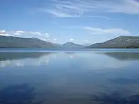 A blue lake with three mountains in the background and a mostly clear sky