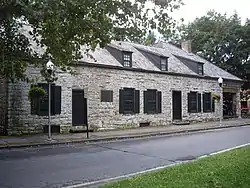 A one-story stone house with black trim and two lampposts in front.