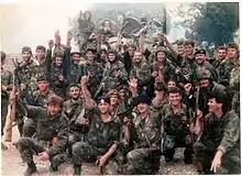 Large group of smiling soldiers, with arms raised