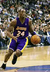 A black player near the basket with mouth open and right arm raised with ball in hand, preparing for a dunk.