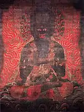 Frontal view of a fierce looking black deity surrounded by flames.
