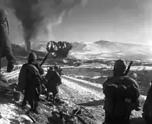 Soldiers watch a hill in front of them as aircraft drop bombs on it