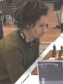 Korley staring at chessboard, with sign labelling the board or player as "47"