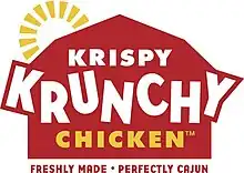 The text "Krispy Krunchy Chicken" in white and yellow letters, on a stylized depiction of a red barn with a yellow sun behind it. Below the barn is the text "Freshly made. Perfectly Cajun." in red letters.