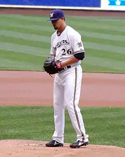 A man in a white baseball uniform and navy cap standing on the pitcher's mound