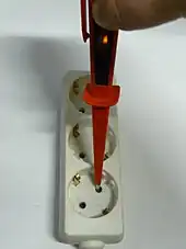 Screwdriver tester inserted in one pin of a European style electrical outlet, with an orange glow visible in the lamp.