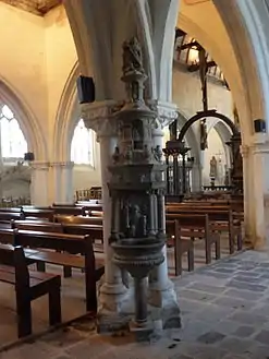 This stoup inside the church has a sculpture at the top depicting Saint Michael fighting the dragon. Over the stoup's basin is a sculpture depicting an angel holding two holy-water sprinklers/aspergillum.("goupillon").