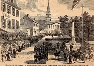 A black and white lithograph of a city square, a stone obelisk and large formations of militia soldiers in dark uniforms parading past the monument