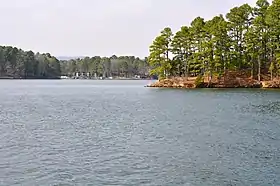 The blue waters of Lake Catherine with a tall pine tree-covered point jutting out into it and camp facilities visible on the shore in the background