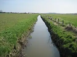 A small, deep, and still watercourse between two green fields