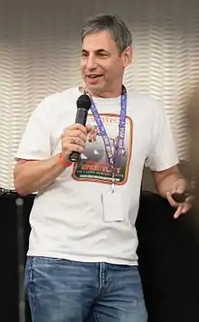 A man wearing a white t-shirt speaking into a handheld microphone