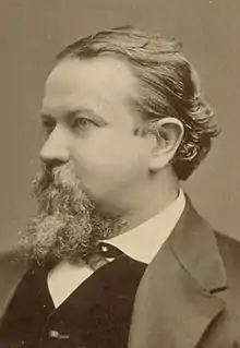 A man with a goatee and slicked-back hair wears a stern expression, looking to the left